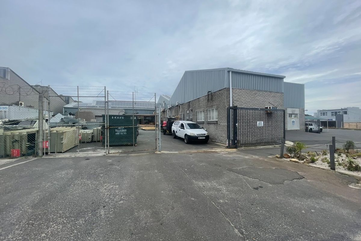 Industrial property exterior featuring a brick and metal facade, secure gated entrance, and paved driveway area.