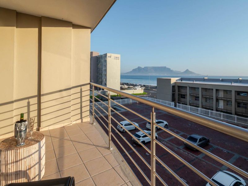 A spacious balcony featuring tiled flooring and a stainless steel balustrade, offering scenic views of the coastline and Table Mountain.