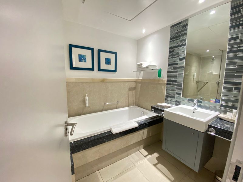 A well-maintained bathroom featuring a built-in bathtub, vanity cabinet with basin, and modern tiled finishes.
