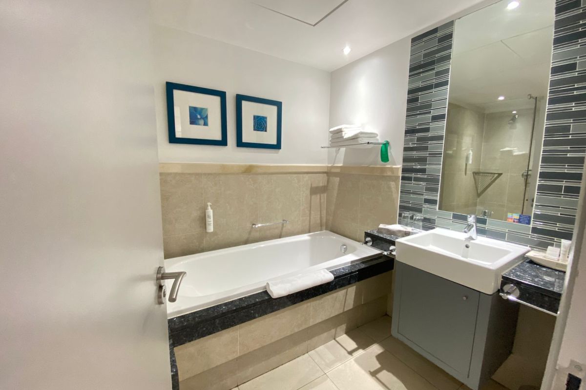 A well-maintained bathroom featuring a built-in bathtub, vanity cabinet with basin, and modern tiled finishes.