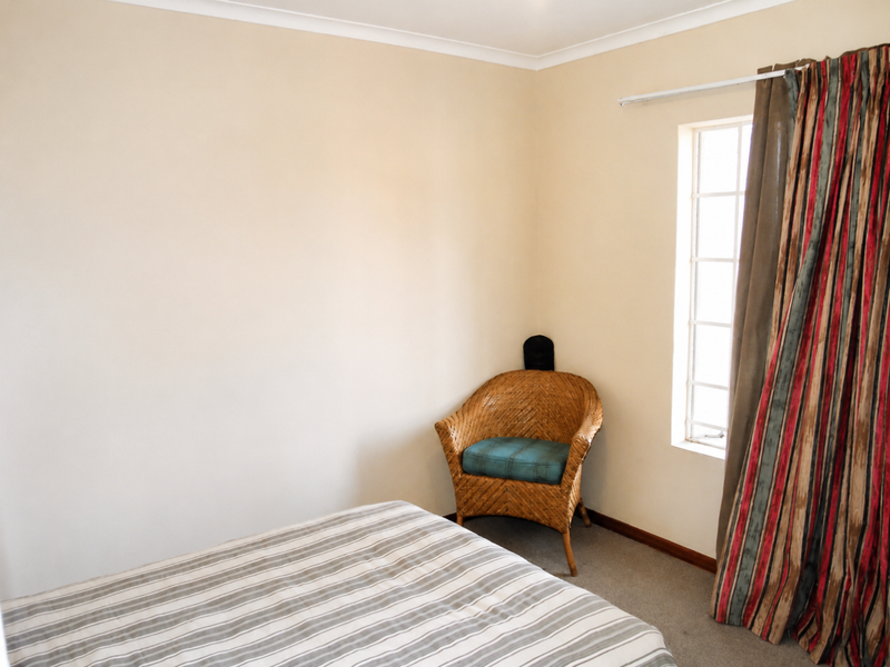 A simple bedroom featuring neutral walls, carpeted flooring, and a window with curtain track.