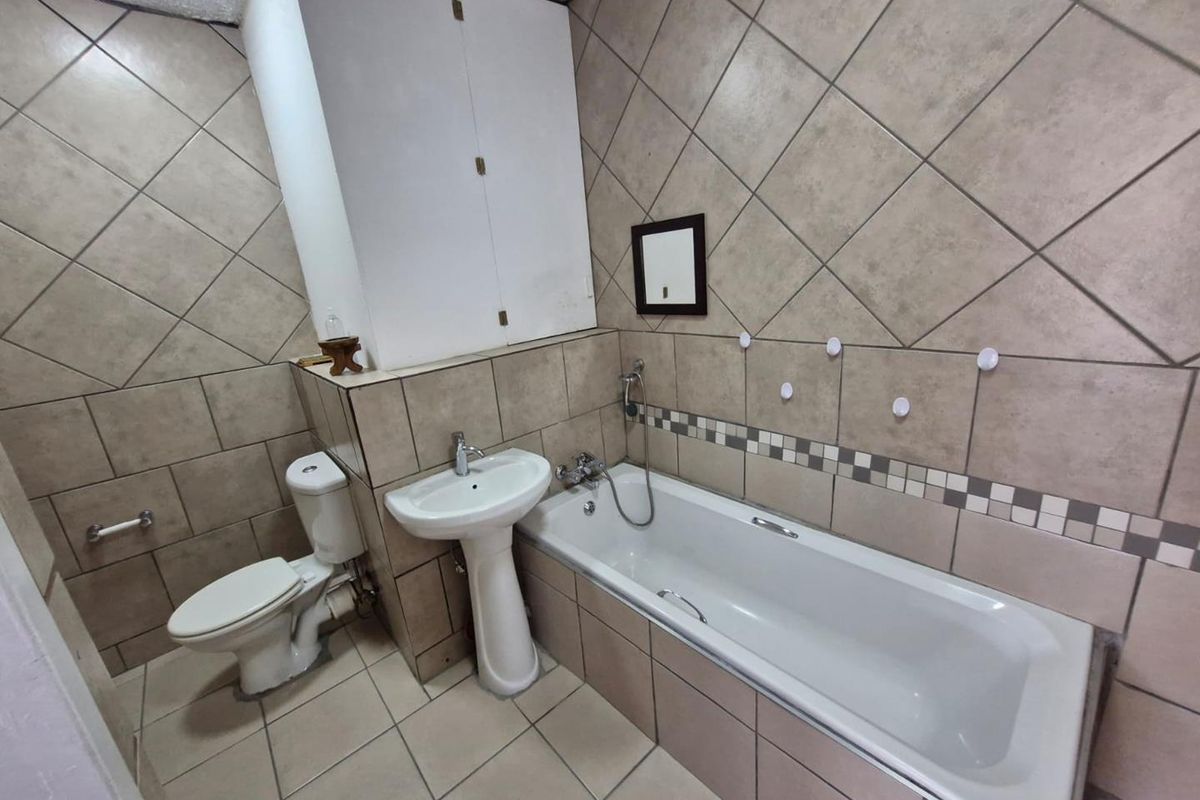 A functional bathroom featuring a pedestal basin, a standard bathtub with shower mixer, and a built-in storage cabinet with full-height wall tiling.