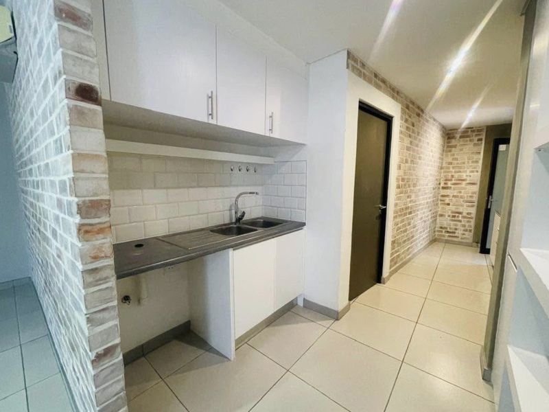 Compact kitchen area featuring white cabinetry, subway tile backsplash, stainless steel sink, and an exposed brick feature wall with tiled flooring.