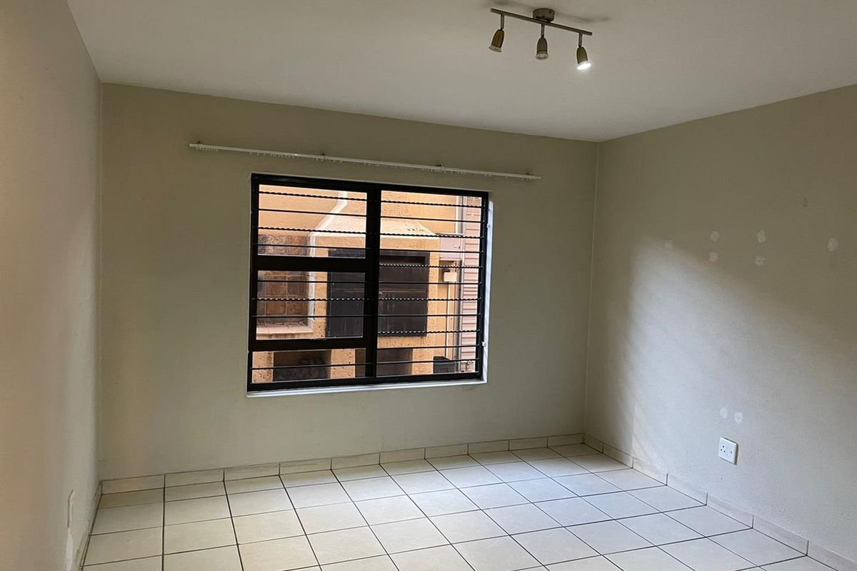An empty bedroom featuring tiled flooring, a window with security bars, and a ceiling-mounted light fixture.