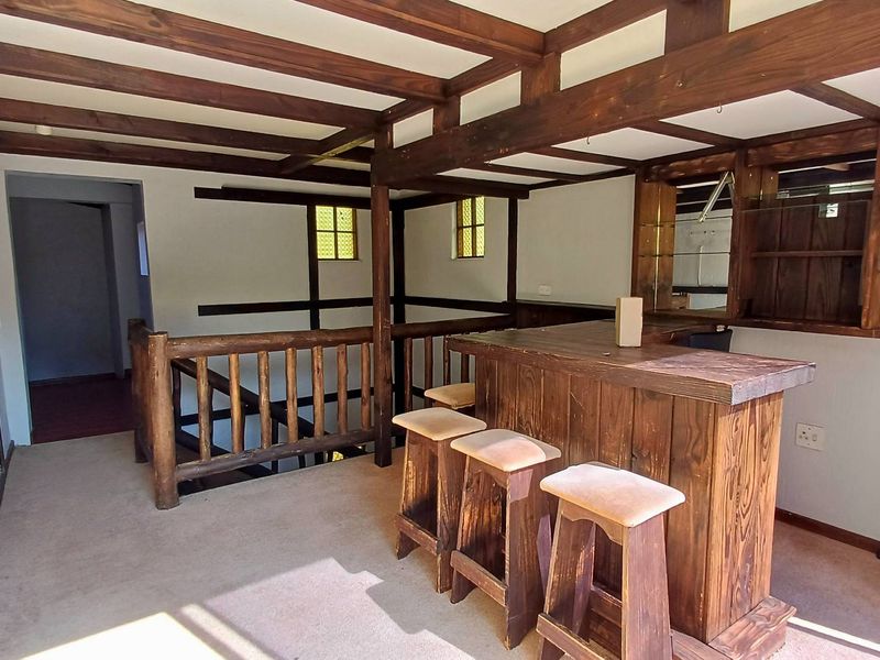 A rustic-style bar area featuring exposed timber ceiling beams, a built-in wooden bar counter, and a timber balustrade overlooking the lower level.