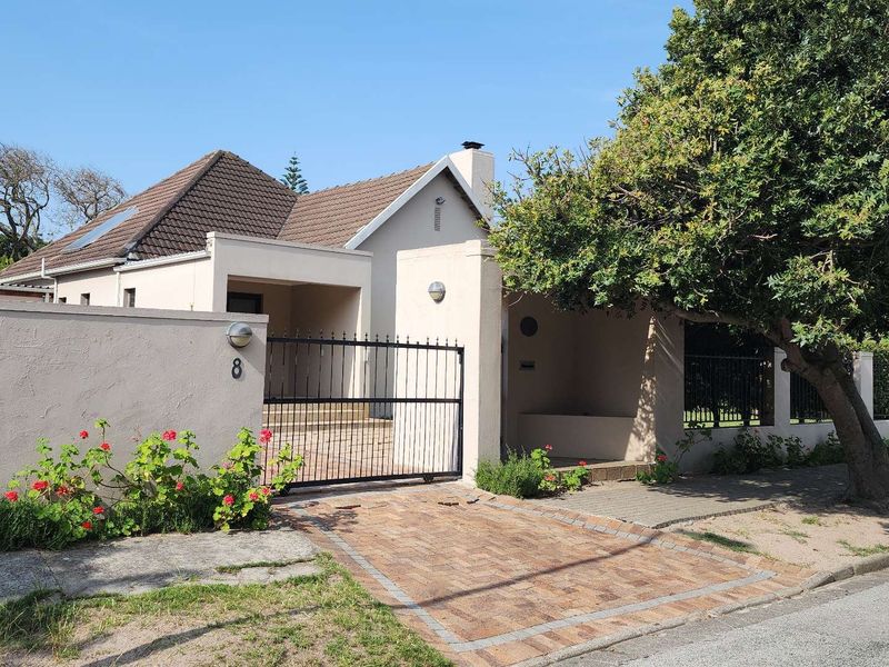 Front view of a residential property featuring a brick driveway, secure metal gate, perimeter wall, and tiled roof structure.