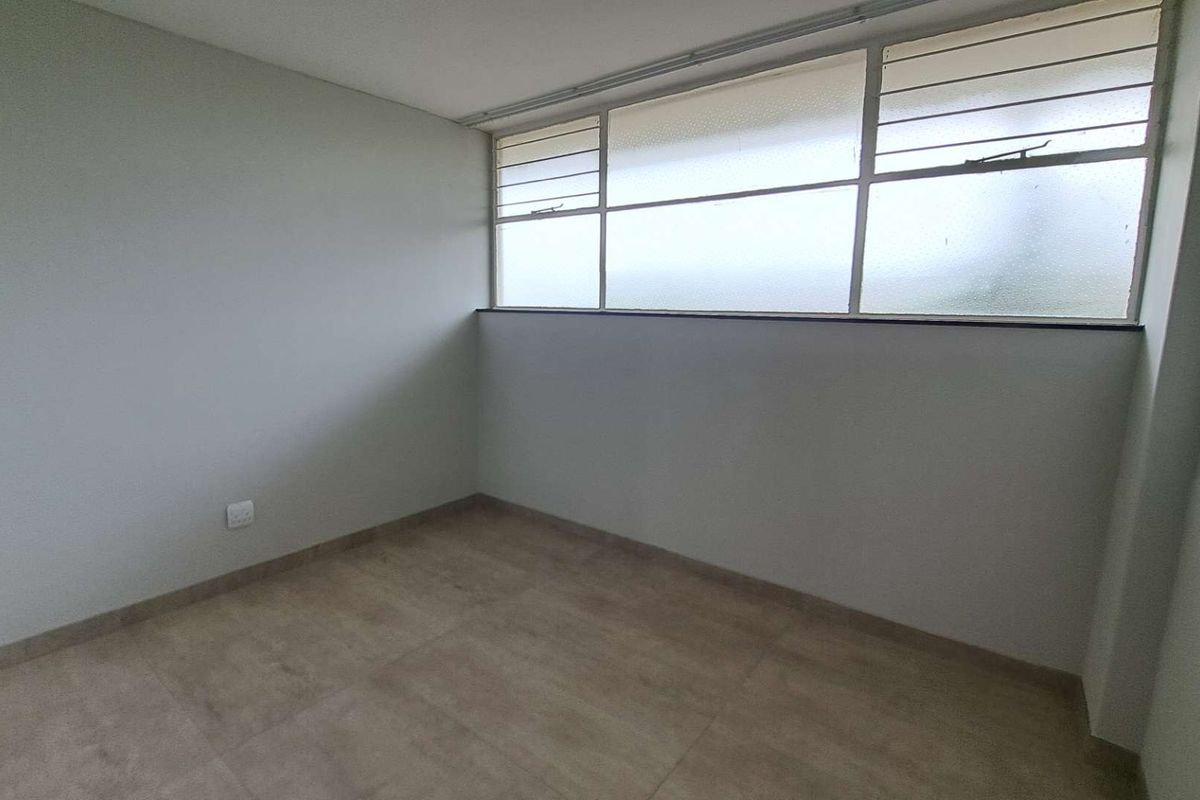 A bright, empty bedroom featuring neutral tiled flooring and large horizontal windows that provide ample natural light.