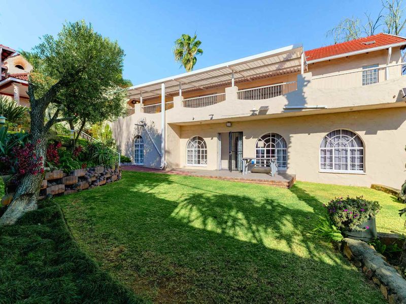 Rear view of the property featuring a landscaped garden, a covered patio area, and distinctive arched windows under a terracotta tiled roof.