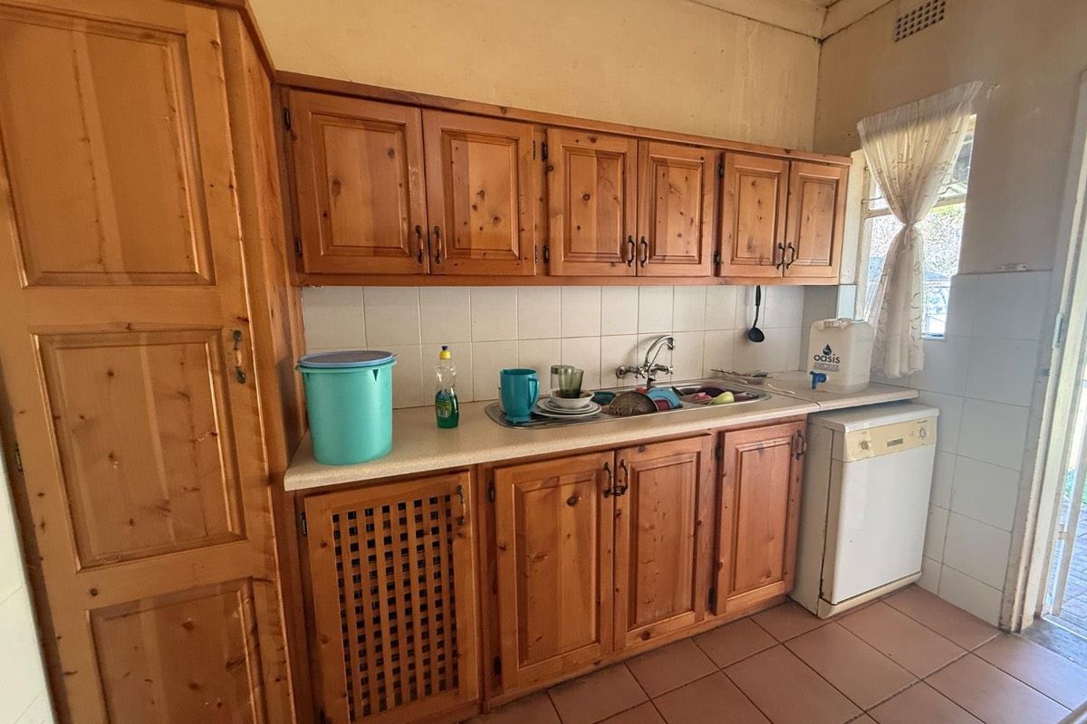 A dated kitchen featuring traditional timber cabinetry, tiled splashbacks, and ceramic floor tiles, offering a functional layout with potential for modernization.