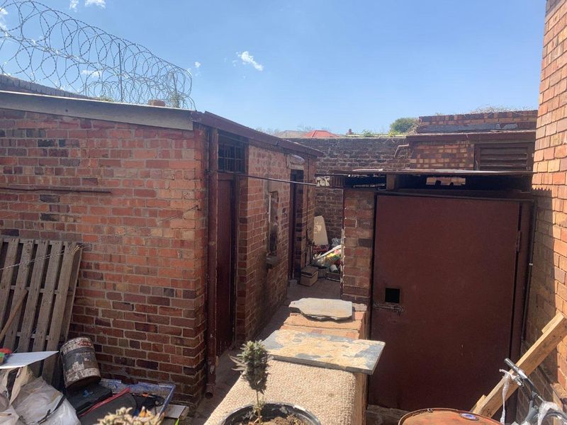Rear exterior view of the property featuring brick outbuildings, metal doors, and perimeter security fencing.