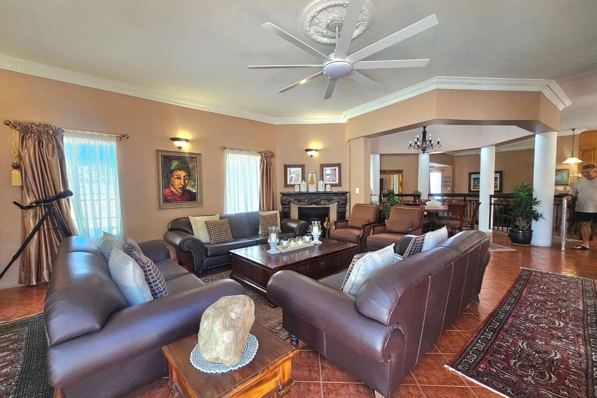 Spacious living room featuring a fireplace, decorative ceiling rose with fan, crown molding, and tiled flooring, opening into an adjacent dining area.