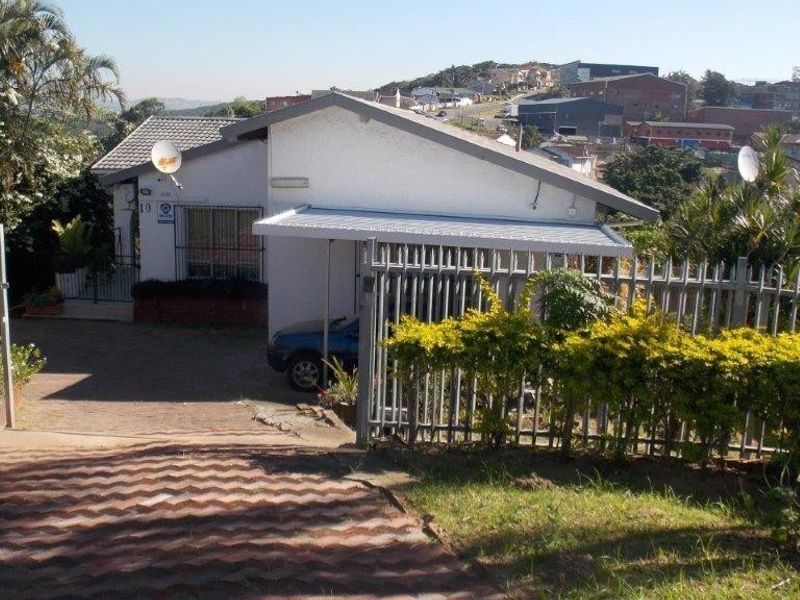 Front view of the property featuring a paved driveway, metal security fencing, and a covered carport area.