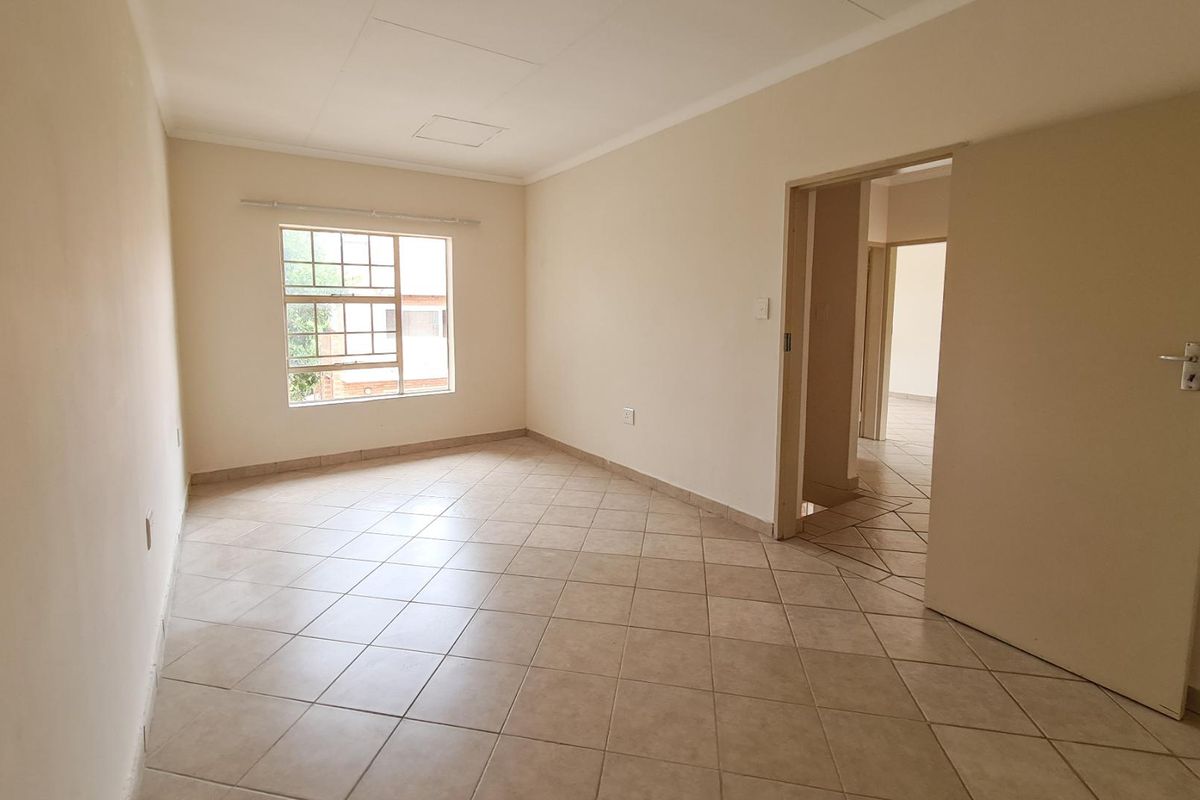 A bright, empty living area featuring neutral tiled flooring, clean walls, and a window allowing natural light, providing a versatile space for customization.