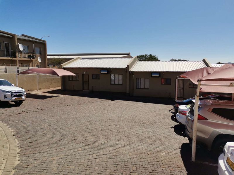 Exterior view of a townhouse complex featuring a paved driveway, covered parking bays, and secure building access points.