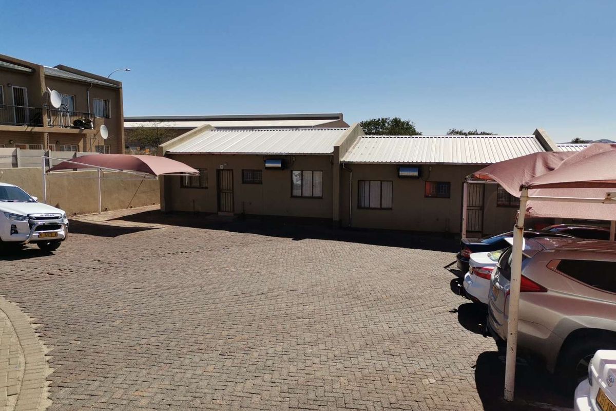 Exterior view of a townhouse complex featuring a paved driveway, covered parking bays, and secure building access points.