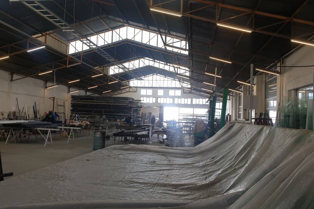 Spacious industrial warehouse featuring high ceilings with exposed steel trusses, skylights, and functional concrete flooring, suitable for manufacturing or storage operations.
