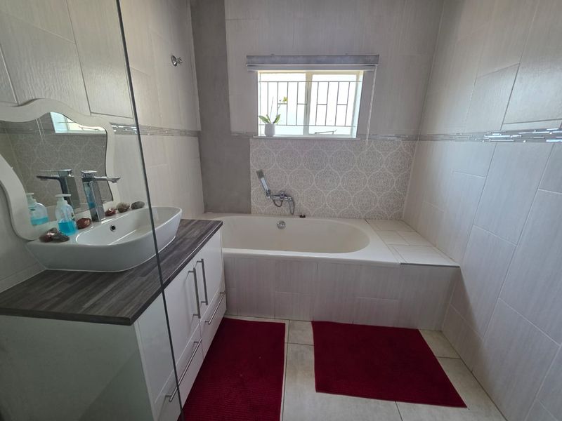 A modern bathroom featuring a built-in vanity with a vessel sink, a bathtub with a handheld shower head, and neutral wall tiling.