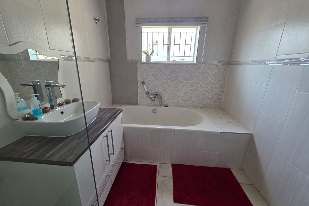 A modern bathroom featuring a built-in vanity with a vessel sink, a bathtub with a handheld shower head, and neutral wall tiling.