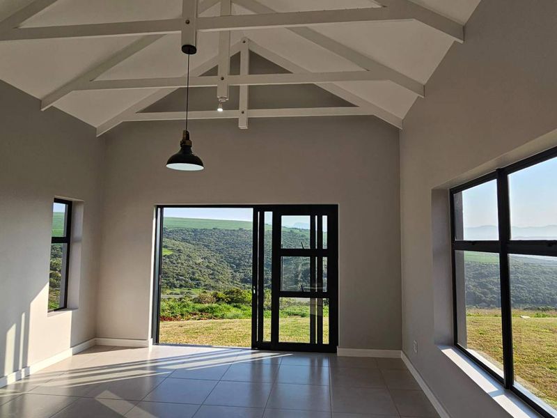 Spacious living area featuring a high vaulted ceiling with exposed trusses, tiled floors, and large sliding doors opening to scenic landscape views.