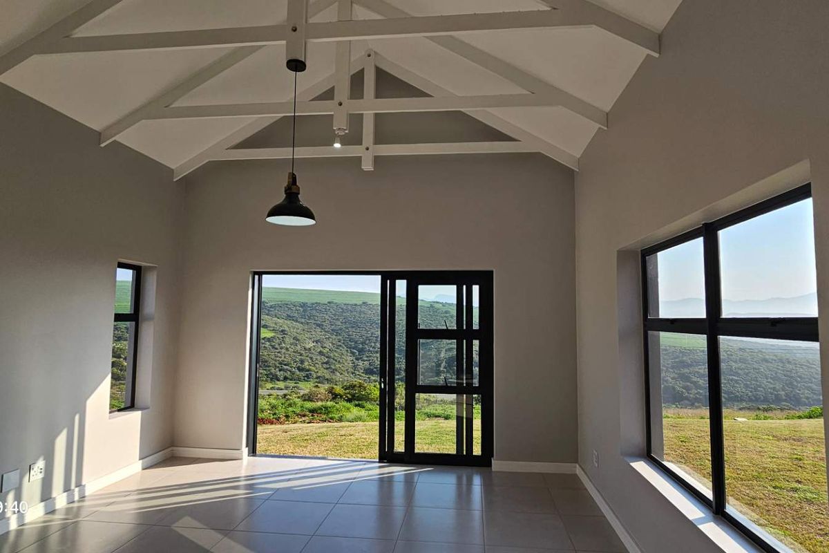 Spacious living area featuring a high vaulted ceiling with exposed trusses, tiled floors, and large sliding doors opening to scenic landscape views.