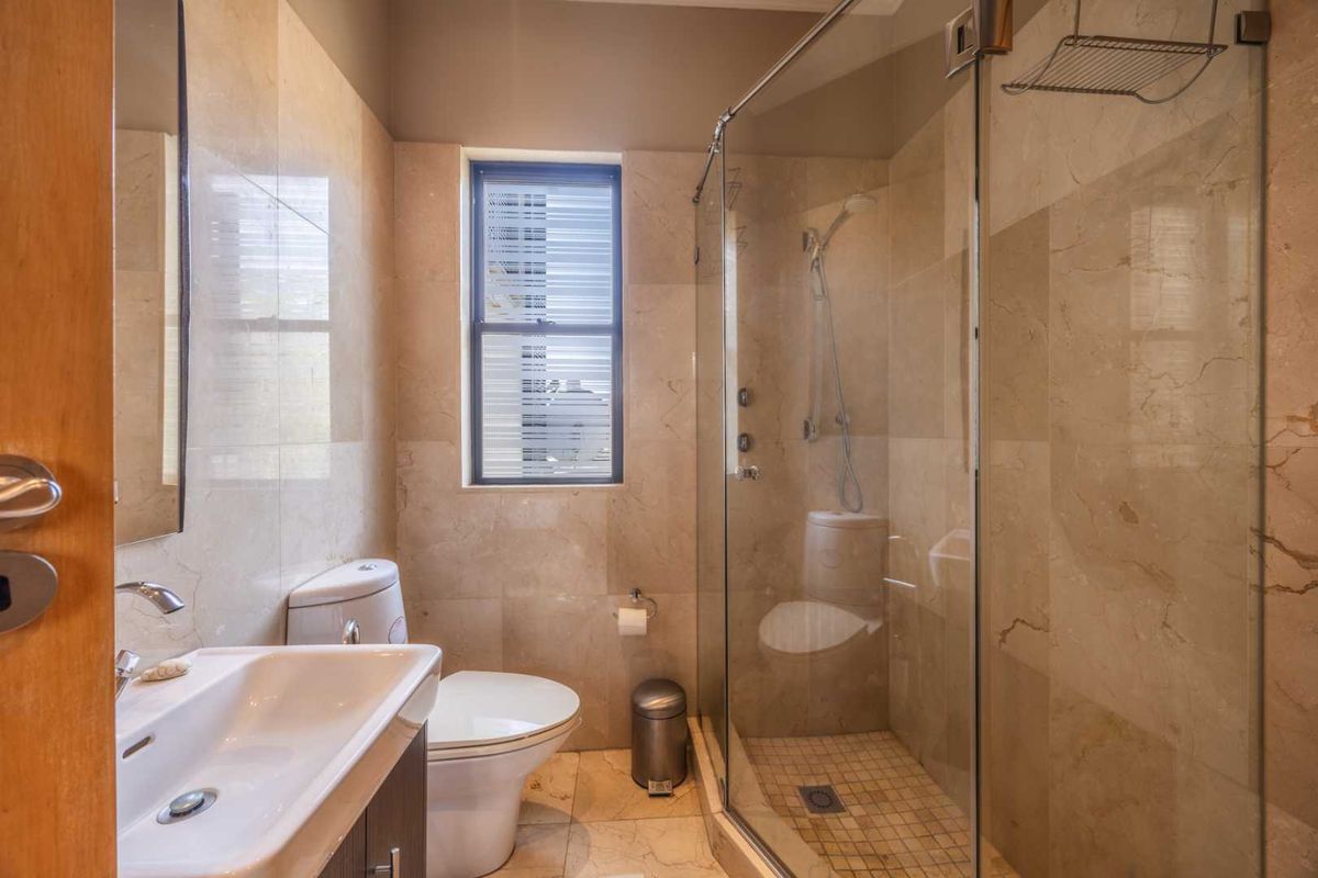 A modern bathroom featuring a glass-enclosed shower, vanity basin, and neutral stone-look wall and floor tiles.