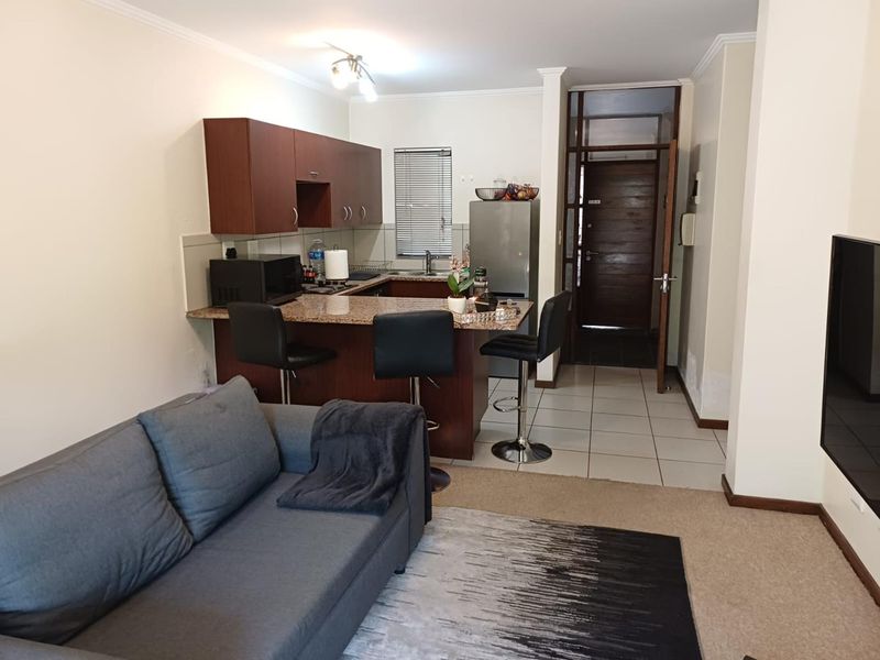 Open-plan living area featuring a kitchen with granite countertops, breakfast bar, and tiled flooring, seamlessly flowing into the carpeted lounge space.