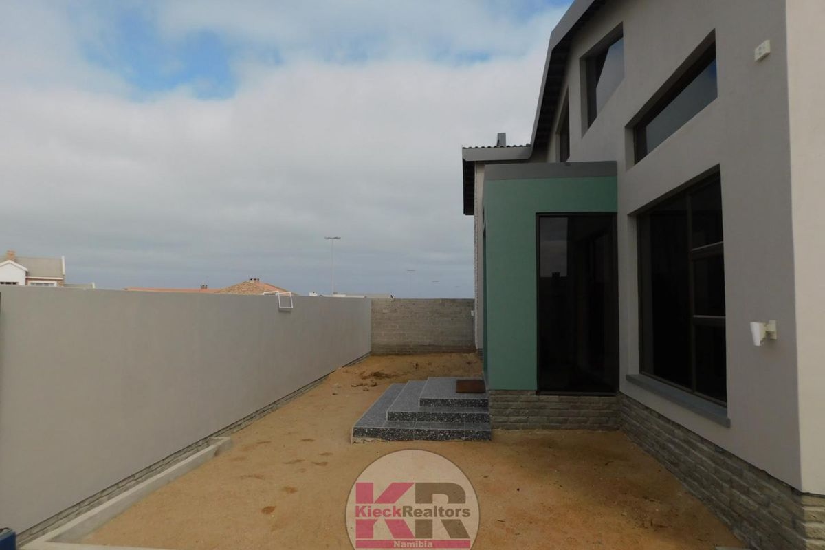 Rear exterior view of the property featuring a paved step entrance, modern grey facade, and an enclosed yard area with unfinished landscaping.
