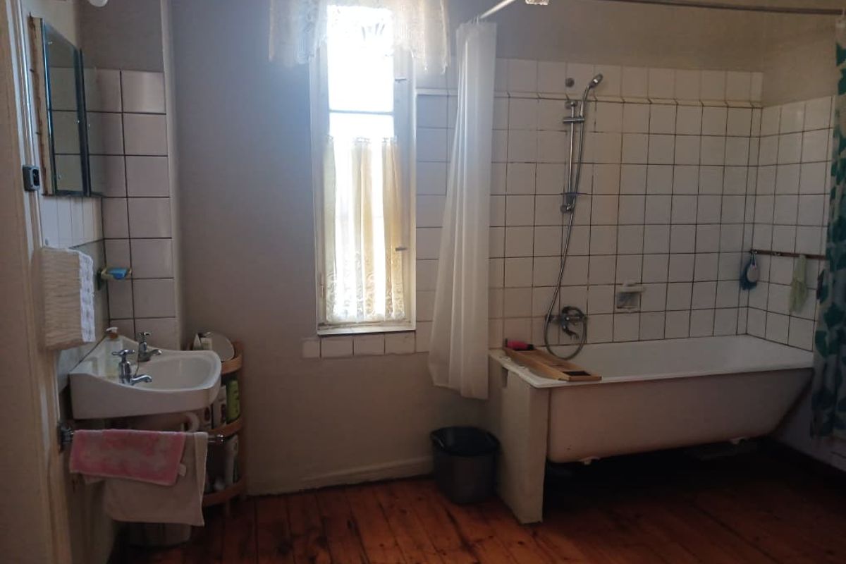 A dated bathroom featuring a wall-mounted basin, bathtub with shower mixer, tiled splashback, and original timber flooring.
