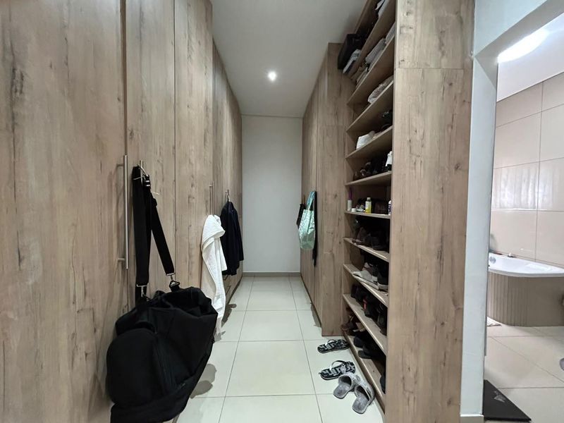 A walk-in dressing area featuring extensive floor-to-ceiling built-in cabinetry with wood-grain finish and open shelving, leading directly into an adjoining bathroom.