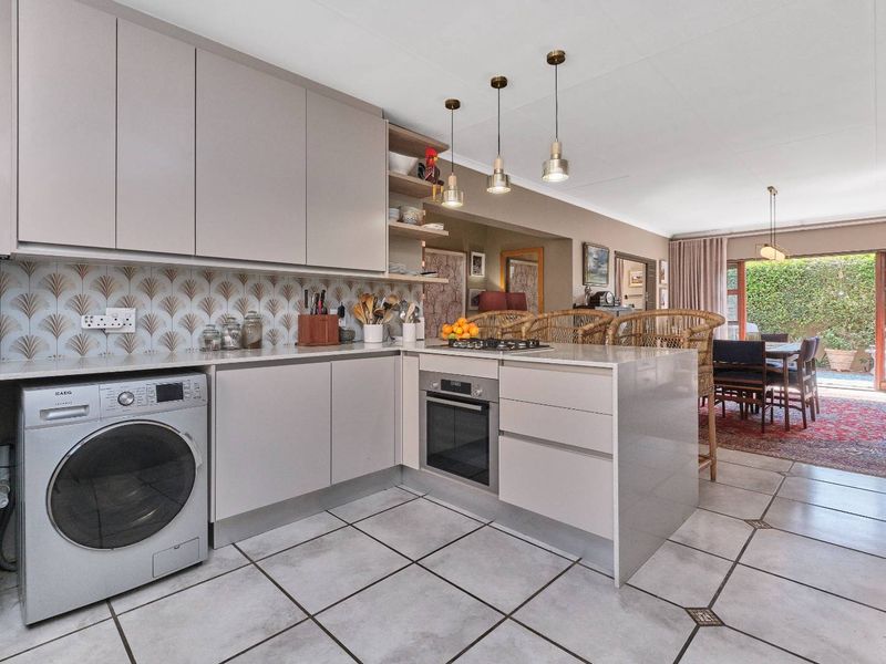 Modern open-plan kitchen featuring sleek cabinetry, stone countertops, integrated appliances, and tiled flooring, flowing seamlessly into the adjacent dining area.