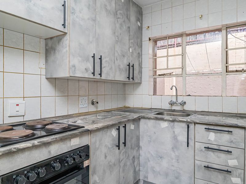 A compact kitchen featuring built-in cabinetry, a laminate countertop, a stainless steel sink, and an integrated electric stove with a tiled backsplash.