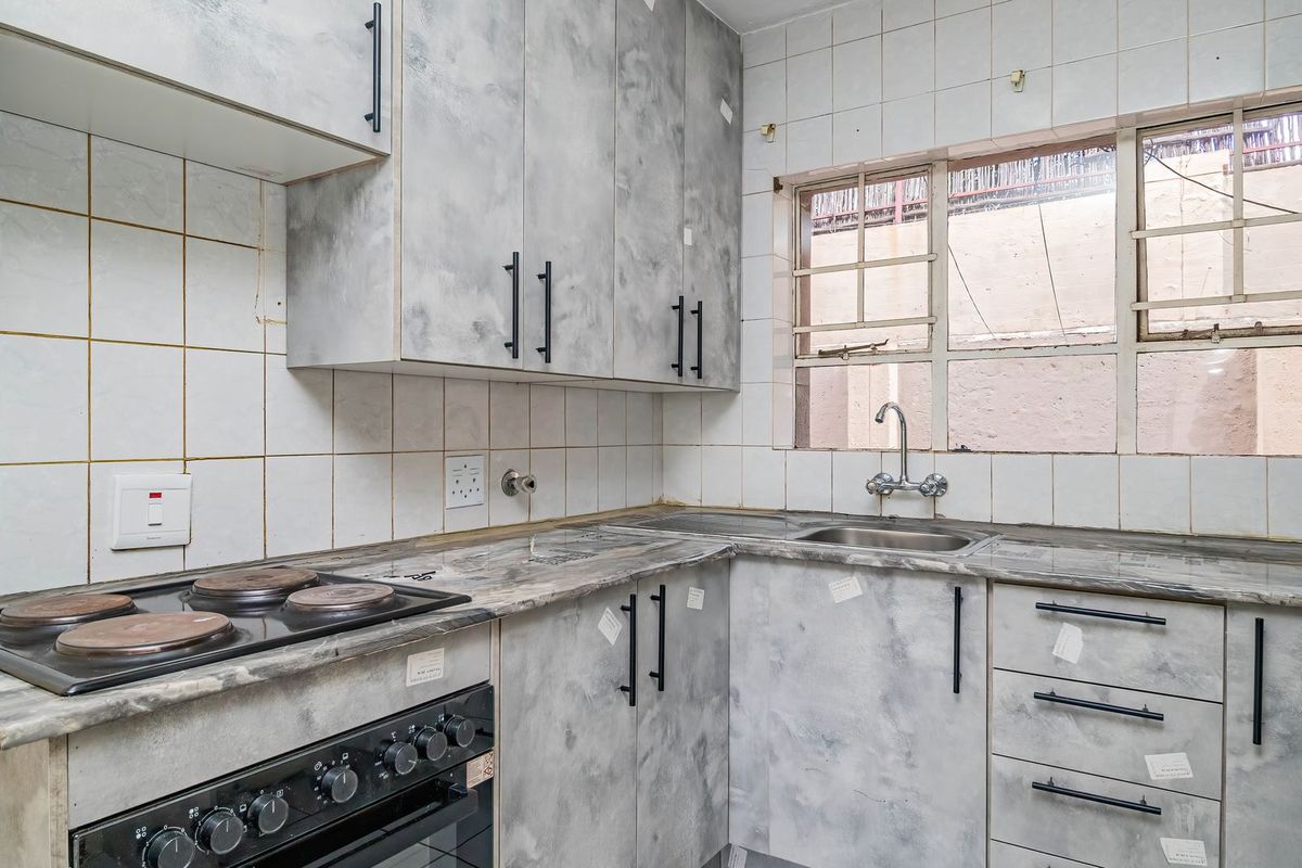 A compact kitchen featuring built-in cabinetry, a laminate countertop, a stainless steel sink, and an integrated electric stove with a tiled backsplash.