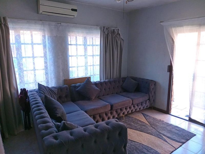 A living room featuring tiled flooring, a wall-mounted air conditioning unit, and access to an outdoor area through a sliding glass door.