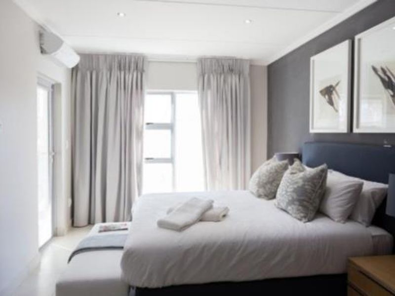 A well-maintained bedroom featuring neutral tones, recessed lighting, an integrated air conditioning unit, and direct access to an outdoor area via a glass door.