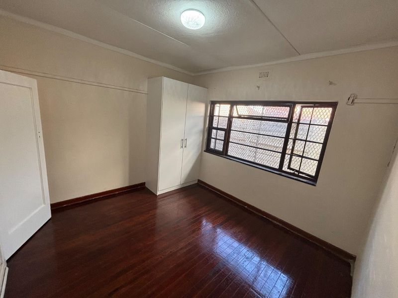 A vacant bedroom featuring polished timber flooring, a built-in wardrobe, and a window fitted with security bars.