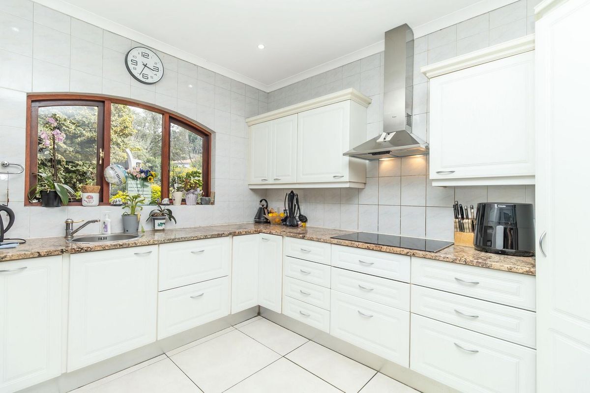 A well-maintained kitchen featuring white cabinetry, granite countertops, a stainless steel extractor fan, and a large arched window providing natural light.