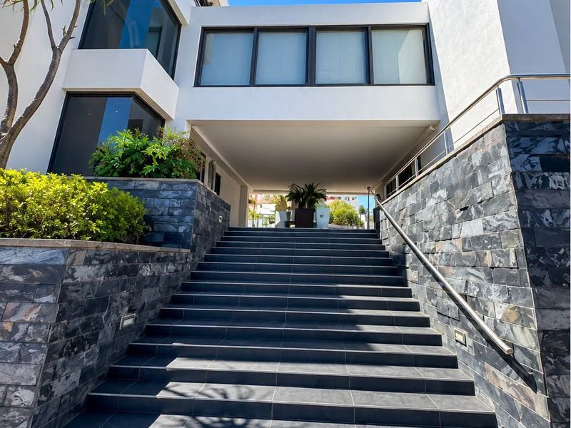 Modern office building entrance featuring a wide tiled staircase with stone cladding, stainless steel handrails, and integrated architectural lighting.