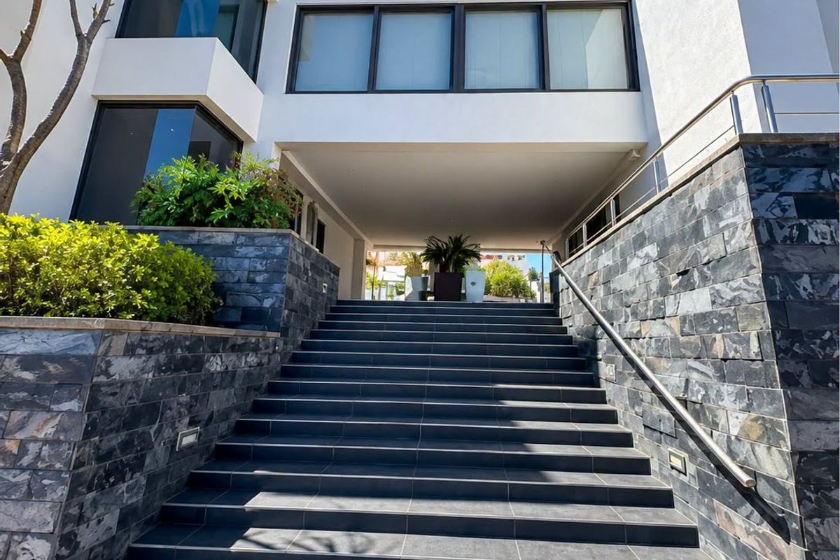 Modern office building entrance featuring a wide tiled staircase with stone cladding, stainless steel handrails, and integrated architectural lighting.