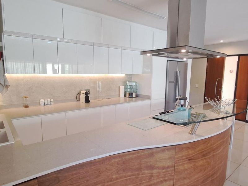 Modern kitchen featuring sleek white cabinetry, stone countertops, a curved breakfast bar, and a stainless steel extractor fan.