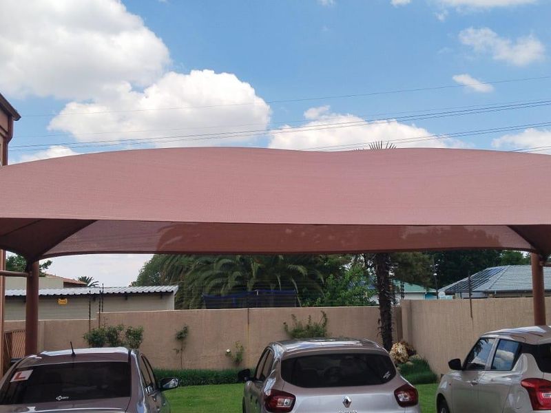 Rear exterior view of the property featuring a shade cloth carport, metal staircase, and a perimeter wall with a lawn area.