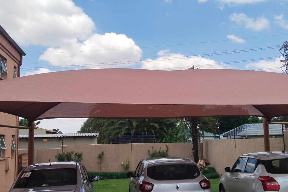 Rear exterior view of the property featuring a shade cloth carport, metal staircase, and a perimeter wall with a lawn area.