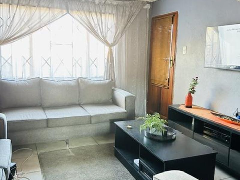 A comfortable living room featuring tiled flooring, a coved ceiling, and a security gate over the window, providing a functional and lived-in space.