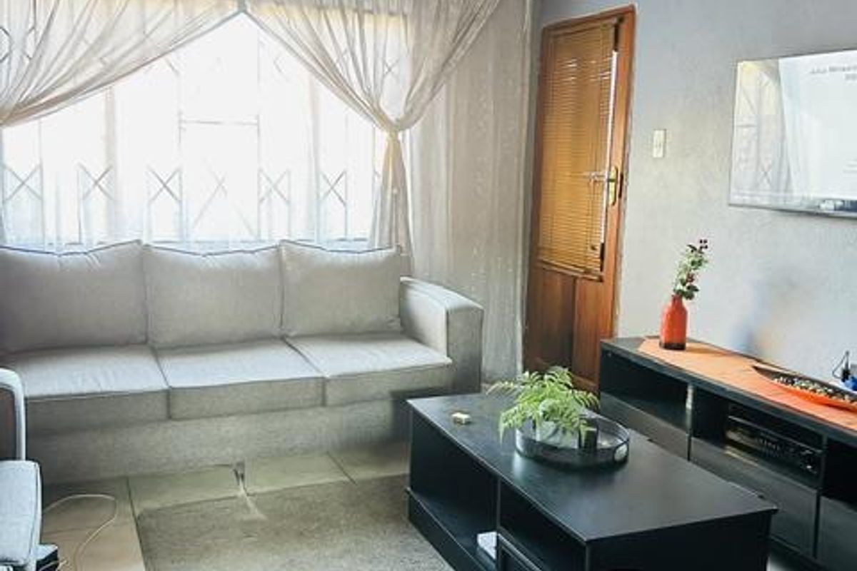 A comfortable living room featuring tiled flooring, a coved ceiling, and a security gate over the window, providing a functional and lived-in space.