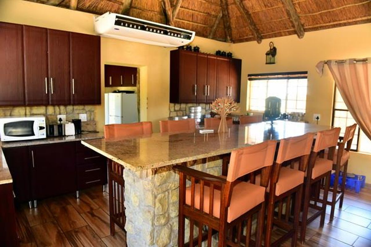 A rustic kitchen featuring dark wood cabinetry, a large stone-clad island with granite countertops, and a traditional thatched roof ceiling.