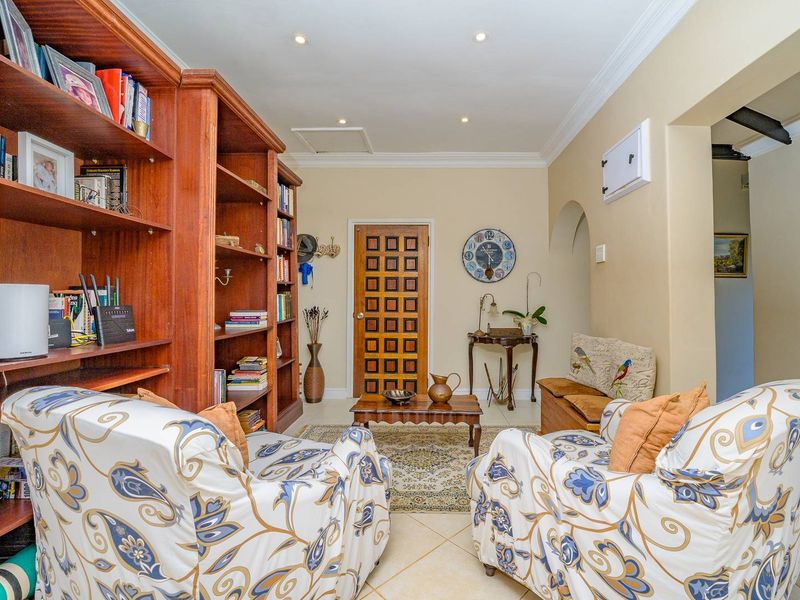 A cozy living area featuring tiled flooring, recessed downlighting, crown molding, and a distinctive timber panelled door with integrated shelving.