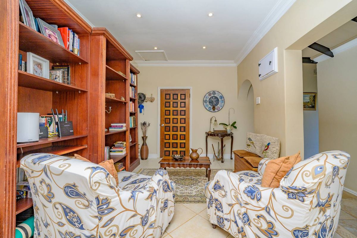 A cozy living area featuring tiled flooring, recessed downlighting, crown molding, and a distinctive timber panelled door with integrated shelving.