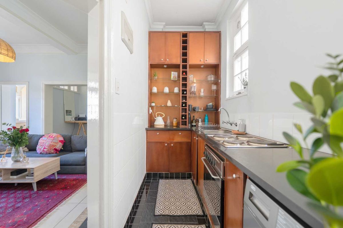 Compact kitchen featuring wooden cabinetry, integrated wine storage, electric hob, oven, and dark tiled flooring, with direct access to the adjacent living area.