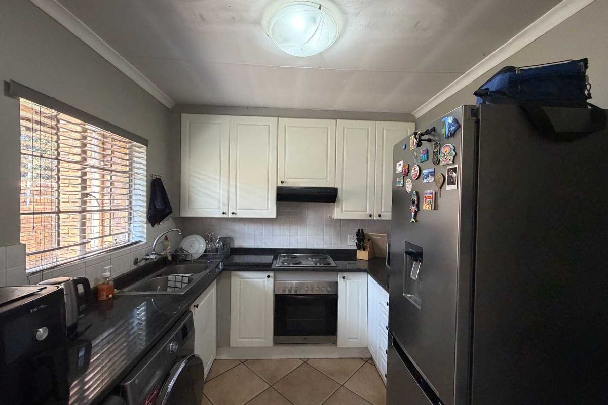 Compact kitchen featuring white cabinetry, dark granite countertops, built-in oven, hob, extractor fan, and a double sink with tiled splashbacks.