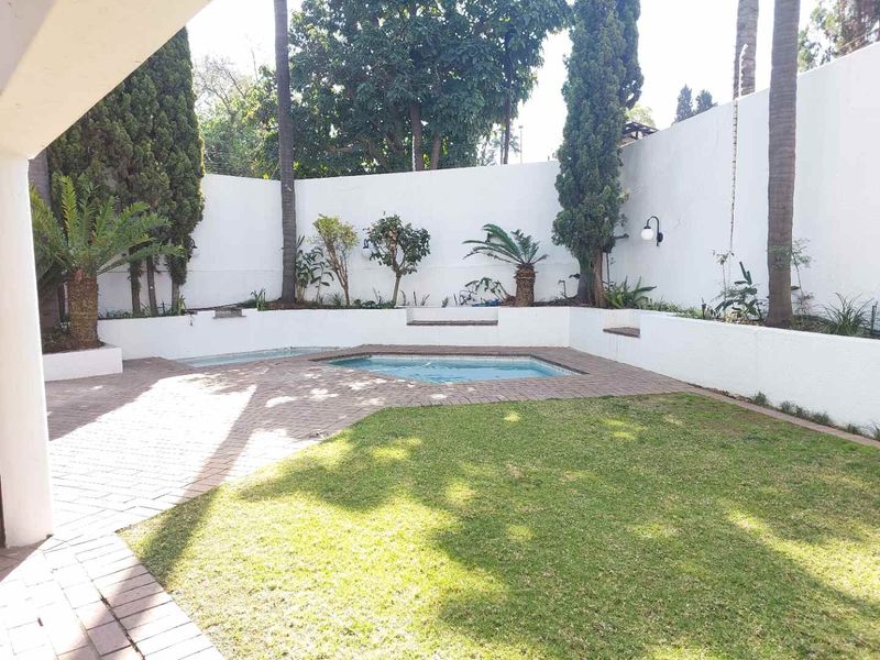 A private outdoor pool area featuring a paved patio, manicured lawn, and perimeter retaining walls with established landscaping.