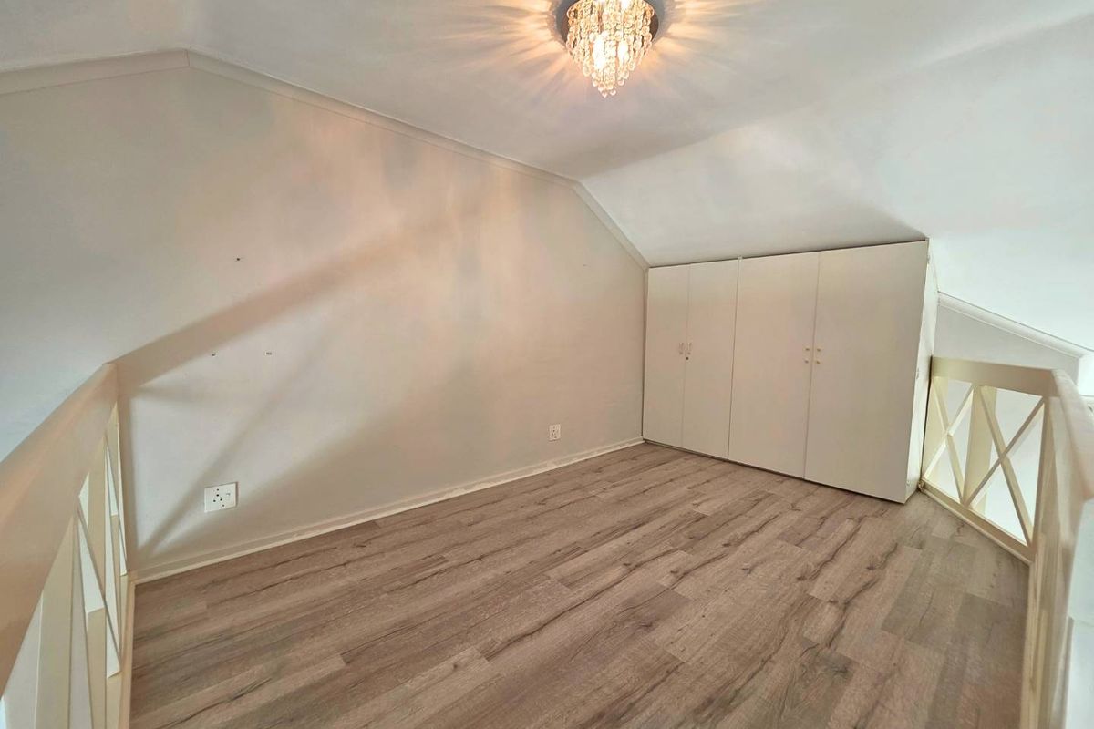 An empty loft-style bedroom featuring laminate flooring, built-in cupboards, and a decorative crystal chandelier under a sloped ceiling.
